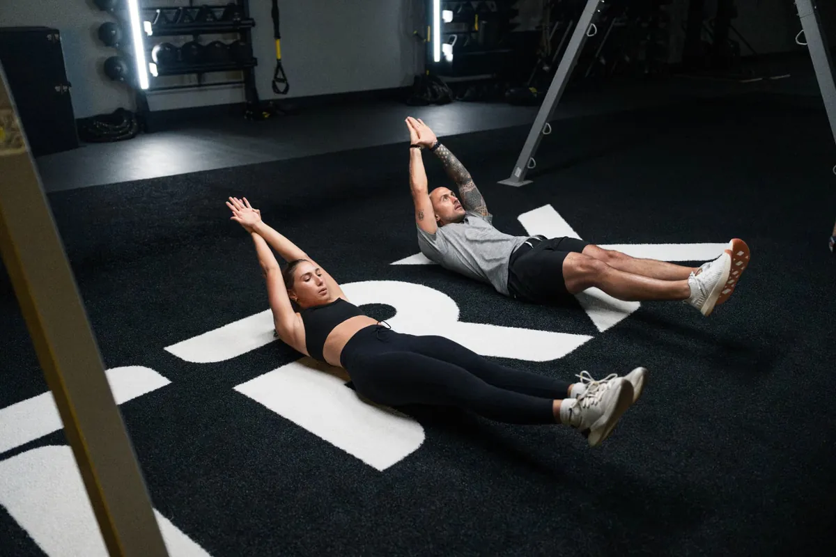 Two members finishing a core exercise side by side on the studio floor