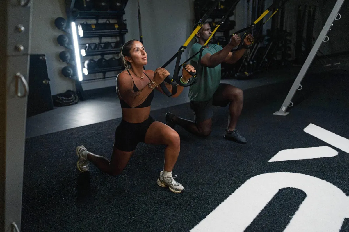 Two members lunging on TRX straps side by side during a Check Fitness workout